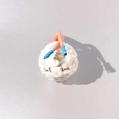 A big Christmas ball decoration with women's legs in blue shoes. Grey  background. Winter holidays in the snow creative concept. Christmas or New Year party card or invitation concept.