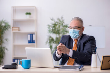 Old male employee working in the office during pandemic