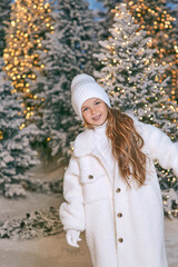 cute caucasian blonde girl in white eco fur coat, hat and gloves walking in the winter christmas forest. New year, fairy tale, fashion concept
