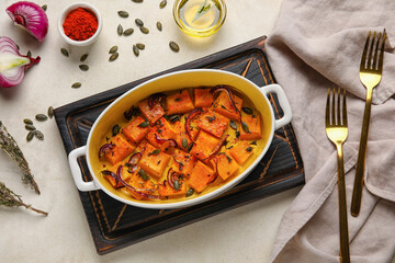 Dish with tasty baked pumpkin pieces on light background