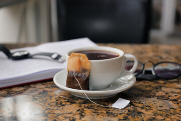 Cup of hot beverage and tea bag on table in cafe