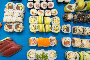 Blue table of assorted sushi, bluefin tuna sashimi, black rice uramaki, uramaki with fresh cheese and masago roe, mango and avocado maki, Norwegian salmon hosomaki, chives and zucchini