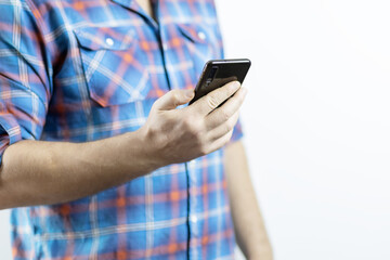 A man in a plaid shirt holds a black mobile phone in his hand on a white background