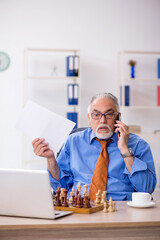 Old businessman playing chess at workplace
