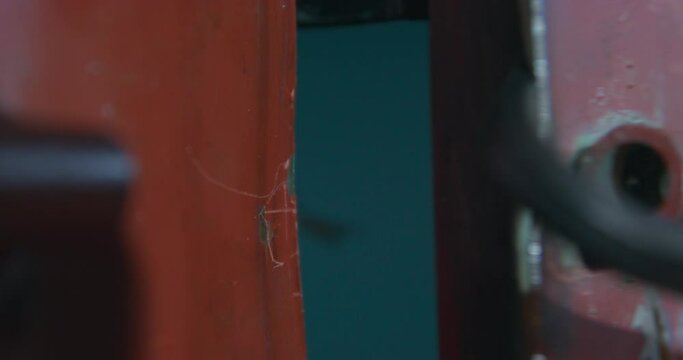 Thief breaks down professionally thick dark red steel door OF storage with help of grey metal pry bar and opens entry closeup