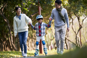 asian parents teaching son child little boy roller skating outdoors in city park