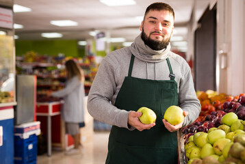 Adult male seller offering ripe apples in grocery shop. High quality photo