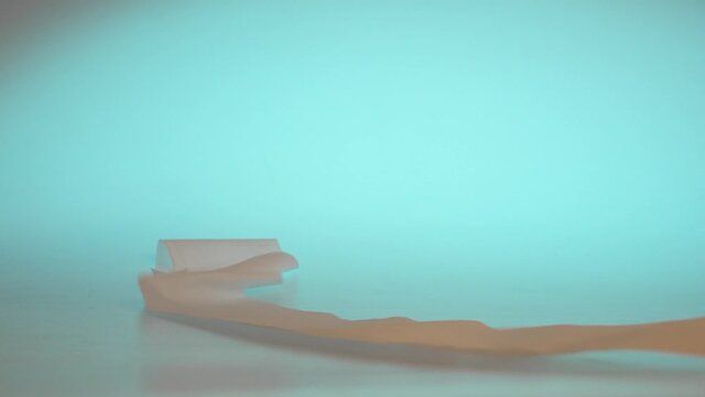 Cinematic slow motion shot of toilet paper rolls dropping onto reflective table top and rolling off the scene, cyan backlit.