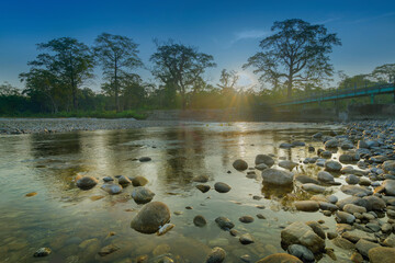 Beautiful sunrise over Murti river, riverbed in foreground with flowing water and stones. Scenic...