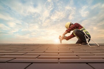 Fototapeta Roofer working in special protective work wear gloves, using air or pneumatic nail gun installing concrete or CPAC cement roofing tiles on top of the new roof under construction residential building obraz