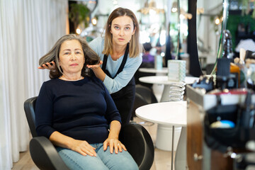 Positive elderly woman visiting professional hair salon. Skilled female hairdresser offering hairstyling to client .