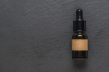 A closed dropper bottle on a black stone background. Flat lay.