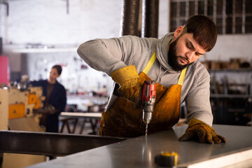 Portrait of confident man mechanic drilling metal sheet in workshop