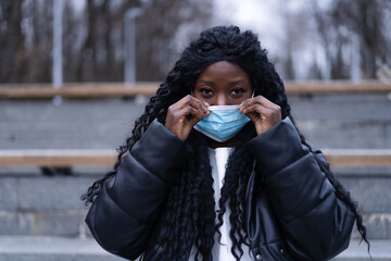 Young Afro girl with face medical mask in a outdoors. African girl using facemask for preventing and stop corona virus spread. Health care people concept