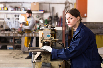 Portrait of young skilled workwoman working on vertical milling machine in metalworking shop....