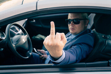 Rude and furious driver giving middle finger to car. A businessman in an expensive car shows an...