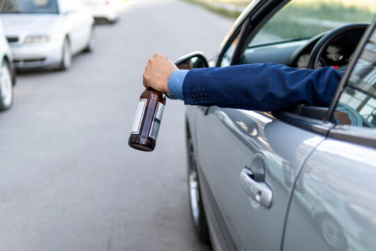 drink and drive. man drinks off a bottle of beer while driving car. concept of alcohol, dangerous driving. driver throws the bottle out of the car window. drunk driving