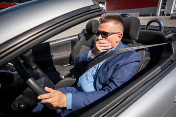 A businessman driving a car covers his mouth with his hand, an emotion of surprise or shock....