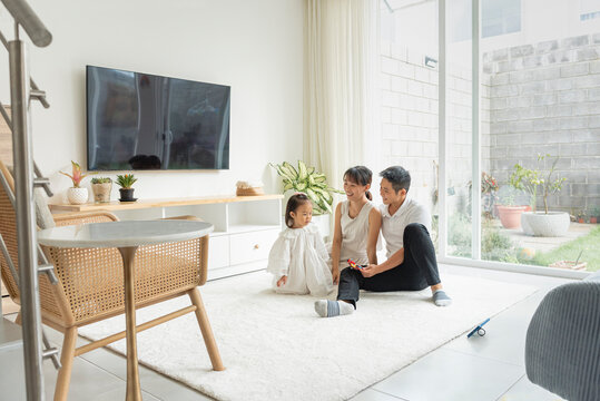 Hermosa familia asiática en su hogar disfrutando un día juntos sentados en la alfombra blanca de su sala 