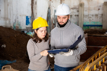 Female architect and young contractor discussing construction plan at building site