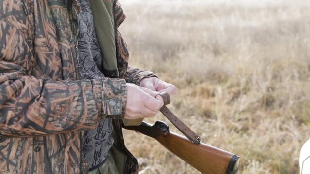 hunter in camouflage is attaching a belt in a double barrel shotgun. senior man with white beard