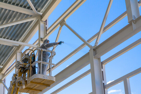 A worker paints metal structures of a building under construction.