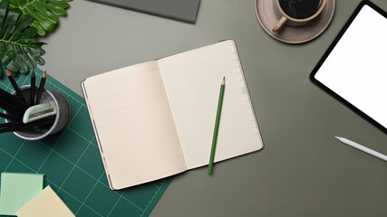 Empty notebook, digital tablet, coffee cup and pencil holder on gray table.