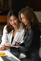 Two female office workers discussing their new project together at office.