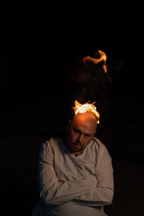 Bald man in a straitjacket with a burning head on a dark background.