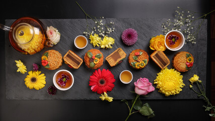 Colourful flower decorated mooncake Chinese mid autumn festival black slate stone background white teacup glass teapot daisy chrysanthemum mum rose baby breath flower red yellow pink purple violet