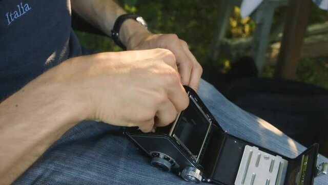 Caucasian man putting a film roll inside an old retro medium format camera.