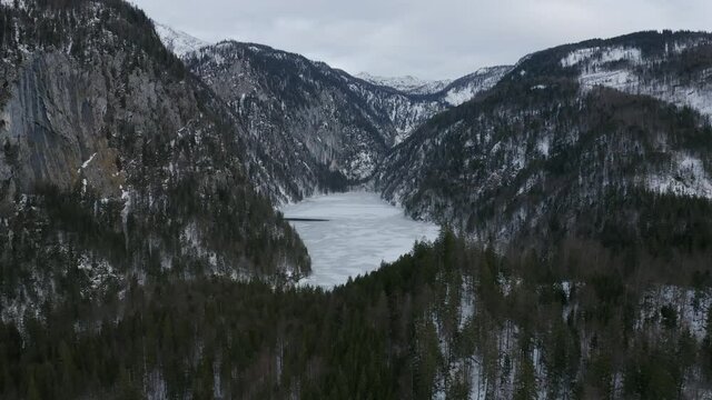 Aerial view moving forward shot, scenic view of Frozen Lake Toplitz Styria, Austria, mountain ranges and white sky in the background.
