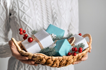 Woman holding basket with sustainable wrapped Christmas gifts, close-up, selective focus. Eco...