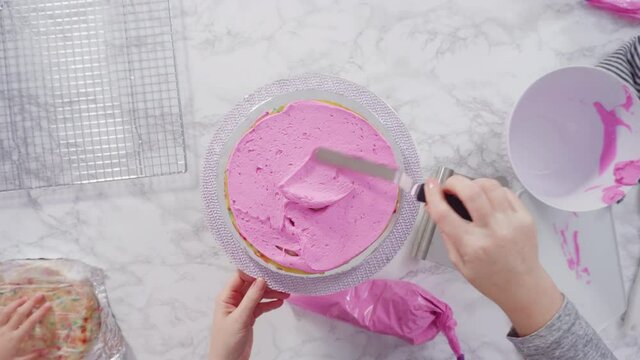Flat lay. Step by step. Frosting round funfetti cake layers with pink buttercream frosting.