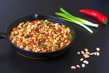 Kung pao chicken in a frying pan on a black wooden table. A traditional, popular dish of Chinese cuisine consisting of chicken, peanuts, hot chili pepper, sauces and spices.