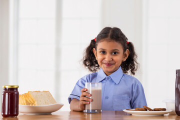 Beautiful Girl in school uniform posing in front of camera while holding a glass of chocolate...