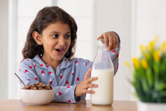 A girl opening cap of a milk bottle to pour into a bowl full of chocos