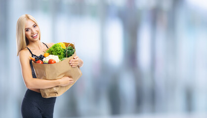 Portrait image of happy smiling young beautiful blond woman holding grocery shopping bag with healthy vegetarian food, shopping mall center purchases, blurred modern interior.