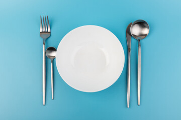 Empty plate with fork and spoon on blue background. Flat lay Dishes for breakfast, lunch or dinner Mock up