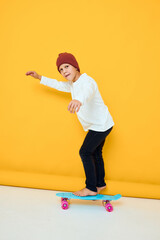 Cheerful little kid in a white sweater skateboard entertainment yellow color background