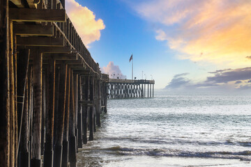 a stunning shot of a long winding brown wooden pier at the beach with vast blue ocean water and...