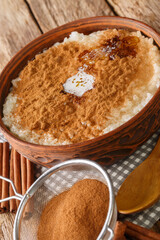 Rice Porridge Risengrod or Risgrynsgrot with sugar, butter and cinnamon close up in the bowl on the table. Vertical