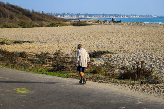 a man in shorts walking along a bike path at the beach with silky brown sand, ocean water and blue sky at Surfers Point at Seaside Park in Ventura California USA