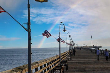a long wooden pier with American flags and curved light posts along the pier with people walking...