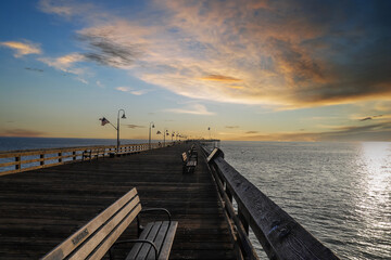 A stunning shot of a long brown wooden pier at sunset with American flags along the edges of the...
