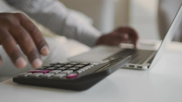 Unrecognizable male african american accountant making financial report online, working on calculator and laptop at home