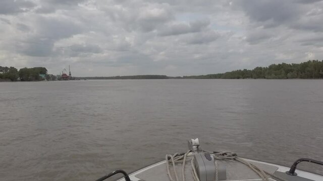 Steadicam shot from bow of sailing boat on the river with port cranes to the left when weather is partly cloudy. Bow of the boat from below and power line from above also