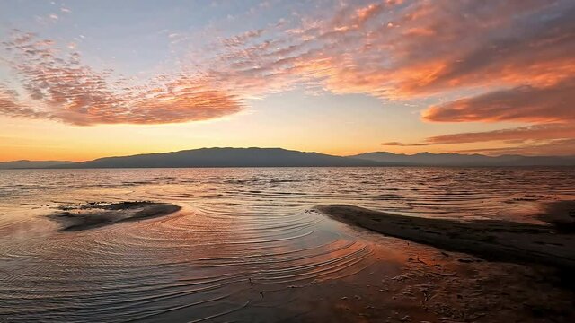 Panning view of colorful sunset reflecting on Utah Lake from the shoreline at Vineyard Beach.