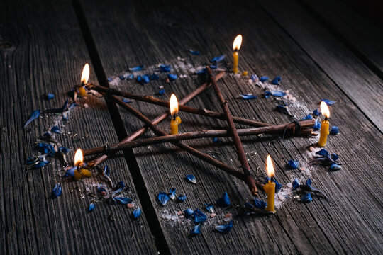 Branch Pentagram - witchcraft tools of natural wood. Wooden pentagram with lighted candles in circle of salt and blue petals. Occultism and mysticism
