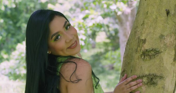 A sexy latina model holds the trunk of a tree while at a tropical park